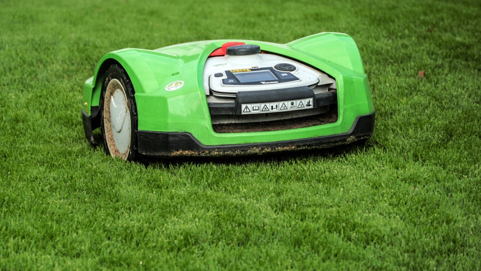 A green robotic mower with two wheels on the side moving across short grass.