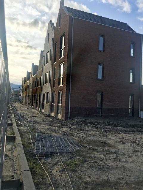 Construction site. Houses on the right on bare, scarred ground, with clouds behind.